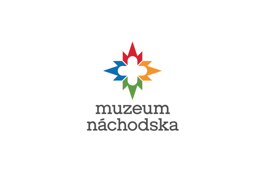 Logo Muzea Náchodska. Tvar střelky kompasu - sever má červenou barvu, jih zelenou, východ žlutou a západ modrou. Pod ní nápis Muzeu Náchodska.