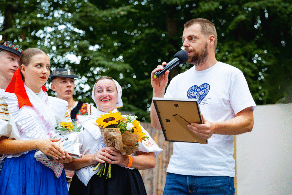 Muž s mikrofonem předává cenu ženám v krojích.