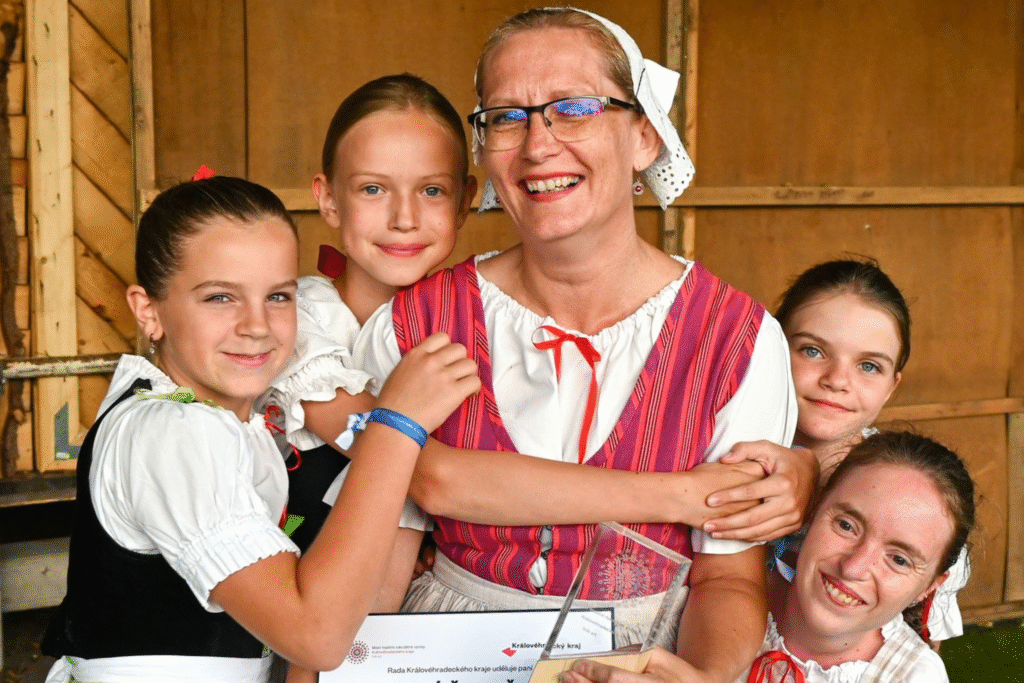 Ženu v kroji s diplomem objímají malá děvčata