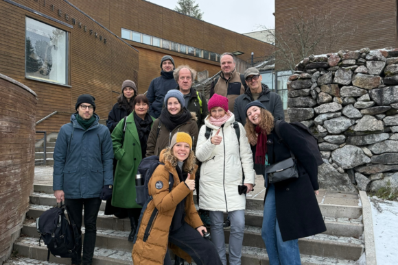 Skupinka lidí stojící na schodech před budovou, smějící se do fotoaparátu