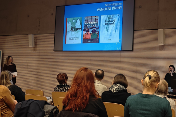 Diváci sledují přenášející o knihách v knihovně.